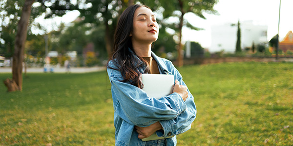 College student relaxing outdoors with her eyes closed and a smile.